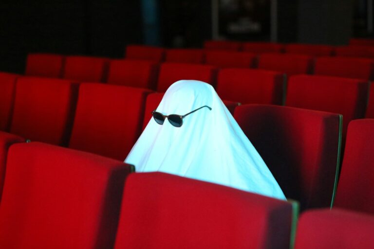 Black Halloween Movies: 69 Best Picks for Spooky Season a ghost sitting in the middle of a row of red seats. halloween