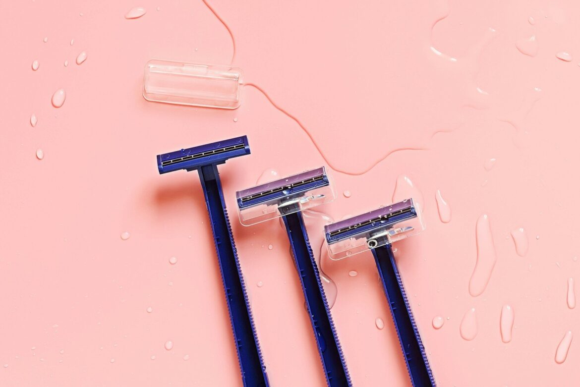 Three blue toothbrushes sitting on top of a pink surface. razor. hair removal.